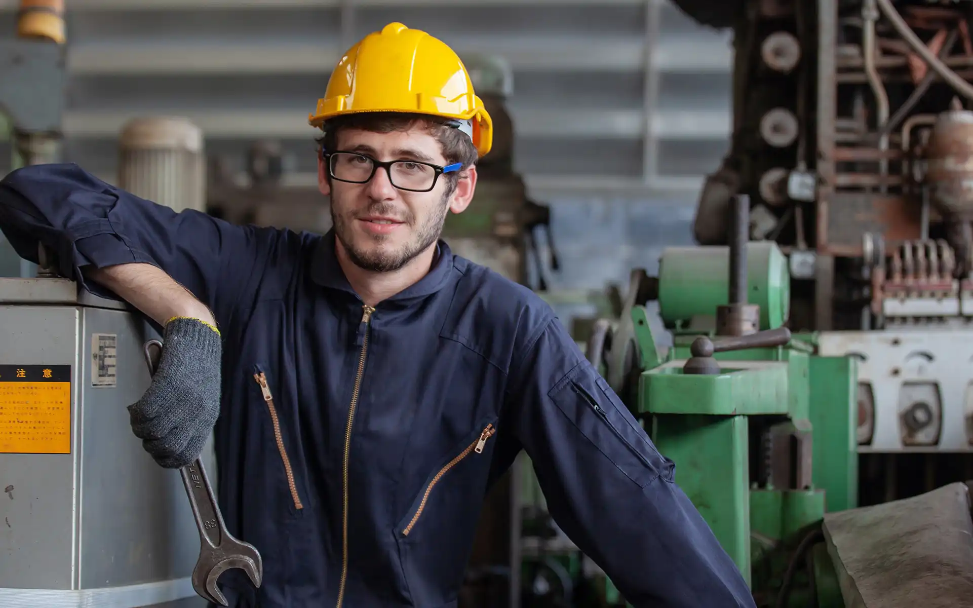 Photo of a man in coveralls and safety helmet holding a wrench